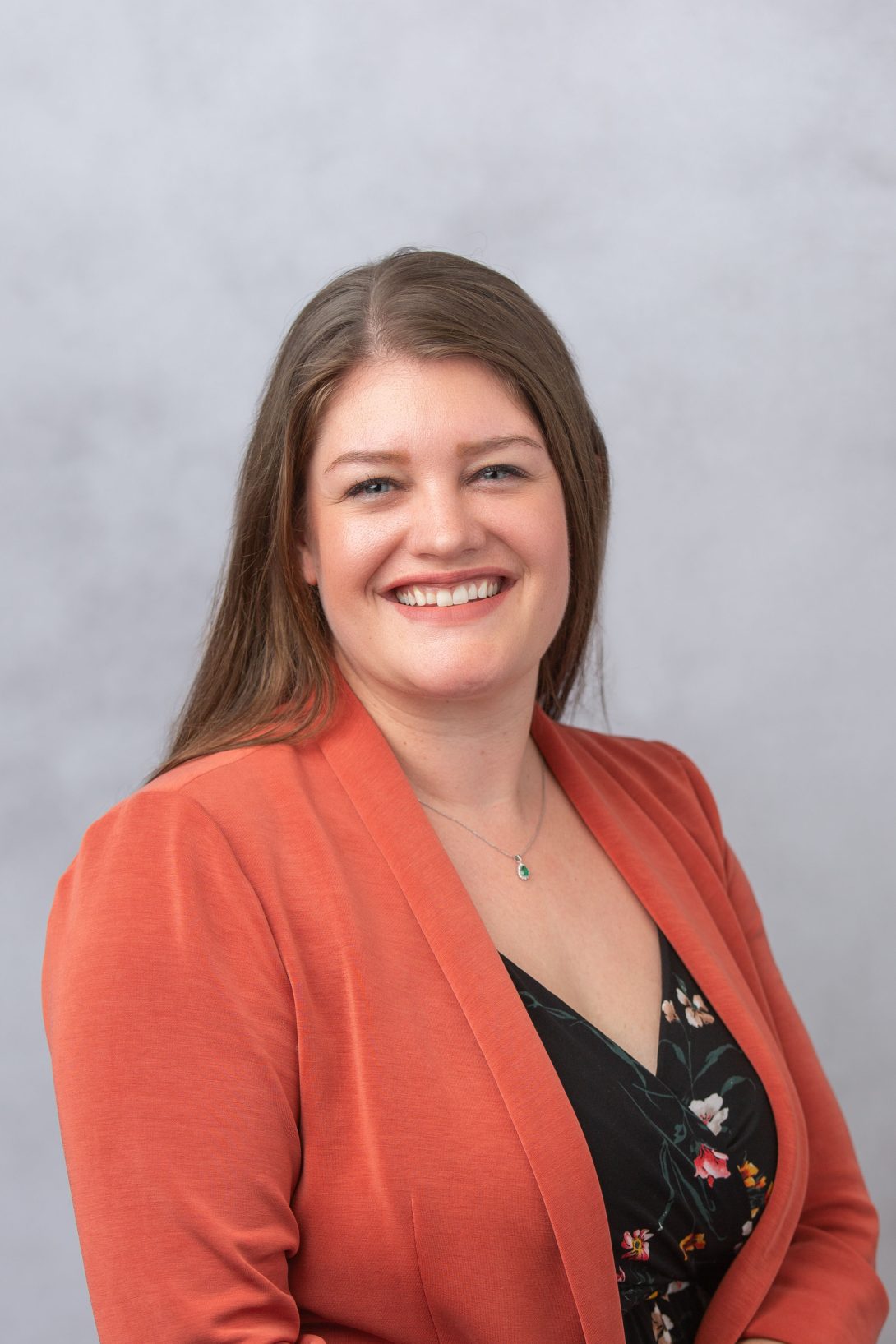Headshot of Postdoc Office Director Valerie Miller, who is wearing an orange blazer and black floral jumpsuit against a gray background