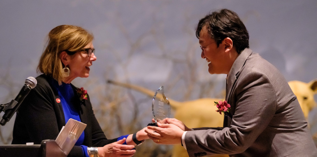 A woman hands a glass trophy to an appreciative man.