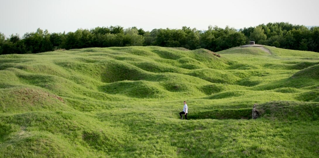 A person stands in a green, hilly field, the site of an infamous World War I battle.