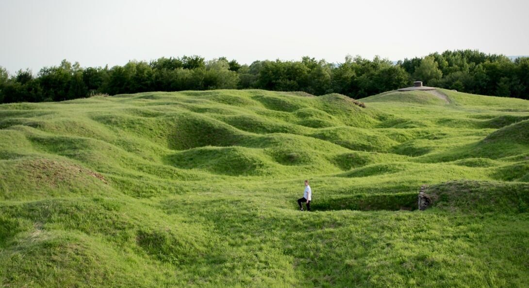 A person stands in a green, hilly field, the site of an infamous World War I battle.