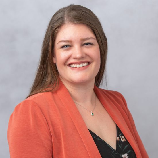 Headshot of Postdoc Office Director Valerie Miller, who is wearing an orange blazer and black floral jumpsuit against a gray background