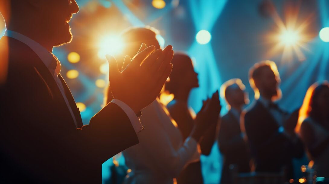 A group of diverse professionals applauding a colleague receiving an award, with a spotlight illuminating the recipient against a blurred corporate setting, celebrating excellence in business.