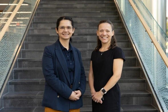 Two women stand on stairs and smile.