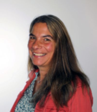 A headshot of a woman in a pink sweater and floral shirt in front of a gray background.