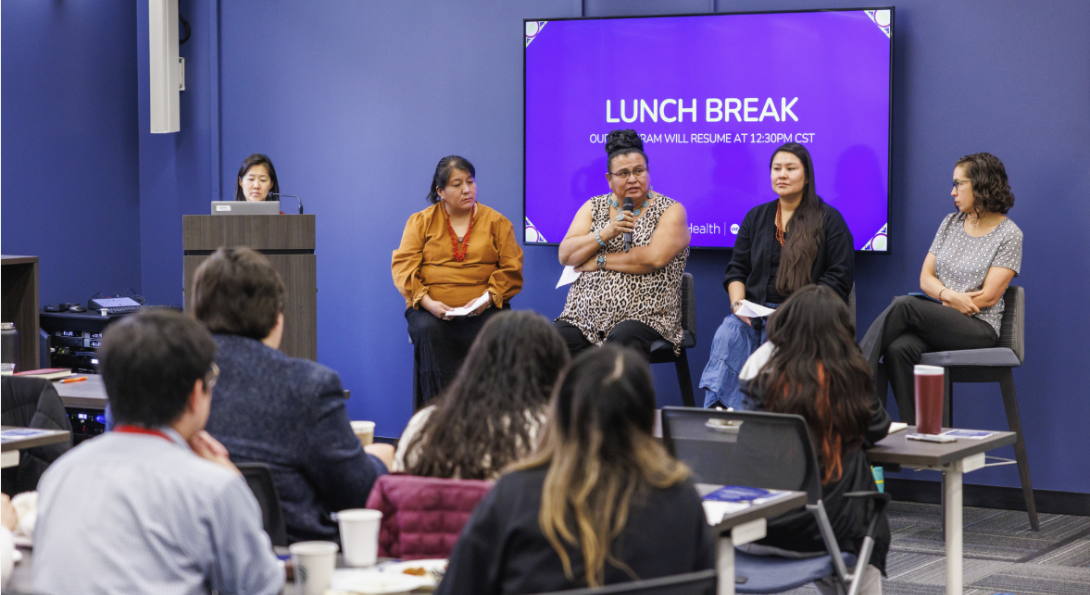 Four women speak on a panel to a crowd.