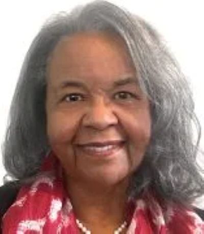 Headshot of a woman with gray hair and a pink scarf against a white background.