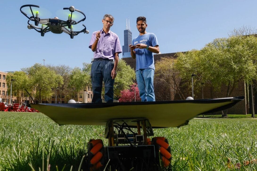 Two male researchers control a drone and ground vehicle remotely in a field.