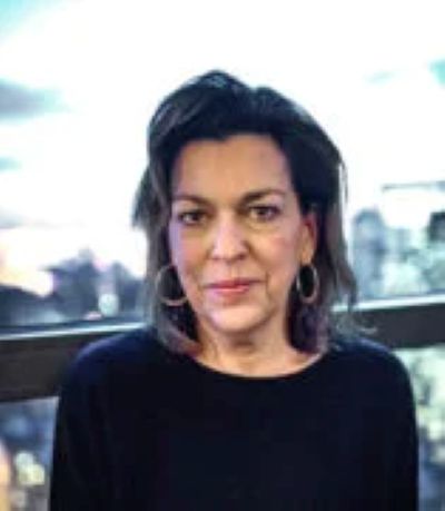 A headshot of a dark-haired woman wearing a black shirt and standing in front of a window