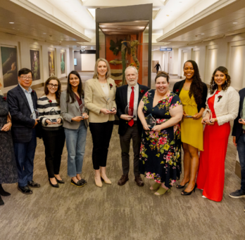 Twelve people stand in a line holding glass awards.
                  